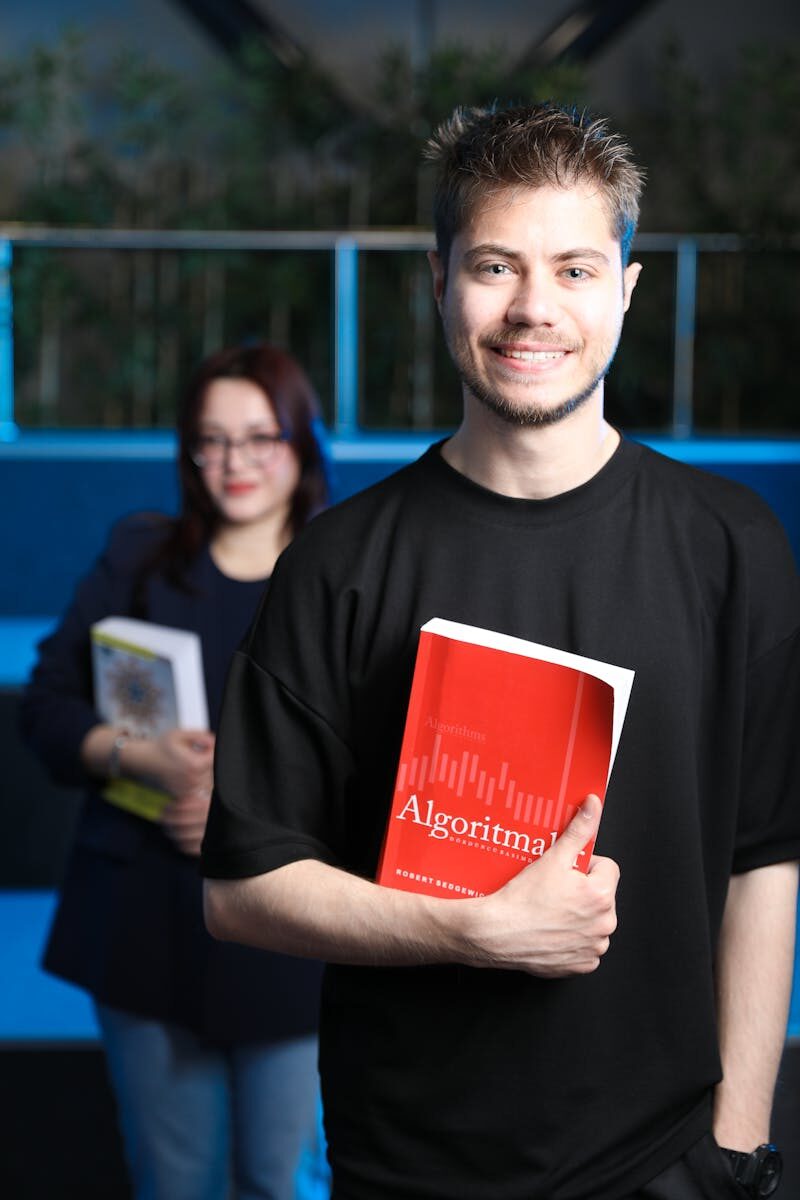 How to Study Abroad for Free — 7 Programs That Cover Everything Two adults holding algorithm-themed books, smiling indoors with a tech-inspired theme.
