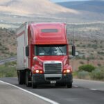 How to Secure Truck Driving Jobs in the USA with Visa Sponsorship: Top 10 Cities to Apply Red semi-truck driving through scenic highway in a mountainous landscape.