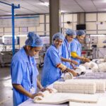 Canada Caregiver & Factory Jobs 2026 $22/hr + Free PR Pathway – Visa Sponsorship for Africans with No Experience. Apply Now Smiling textile workers in a factory sorting and rolling fabrics.