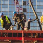 A group of construction workers in safety gear actively working on a high-rise building site.
