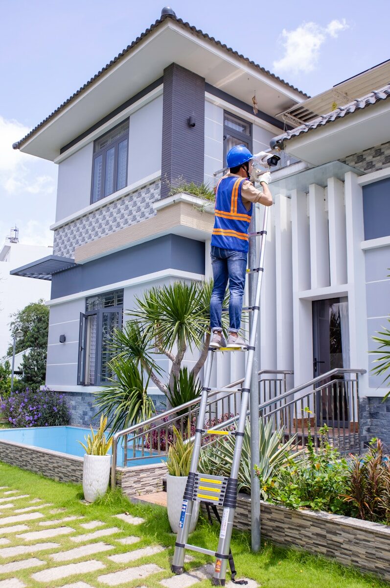man in blue and orange jacket and blue pants standing on white metal ladder during daytime